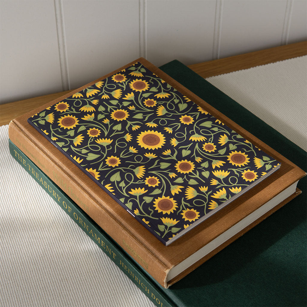 A journal notebook with a botanical sunflower art cover on top of a stack of art books.