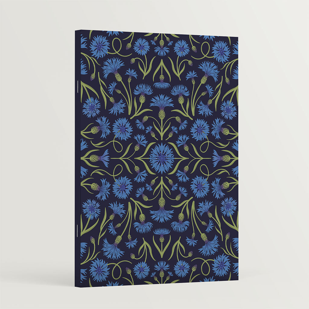 The Heritage Cornflowers Notebook features a vintage-inspired dark cover with a symmetrical pattern of blue cornflowers and green stems.