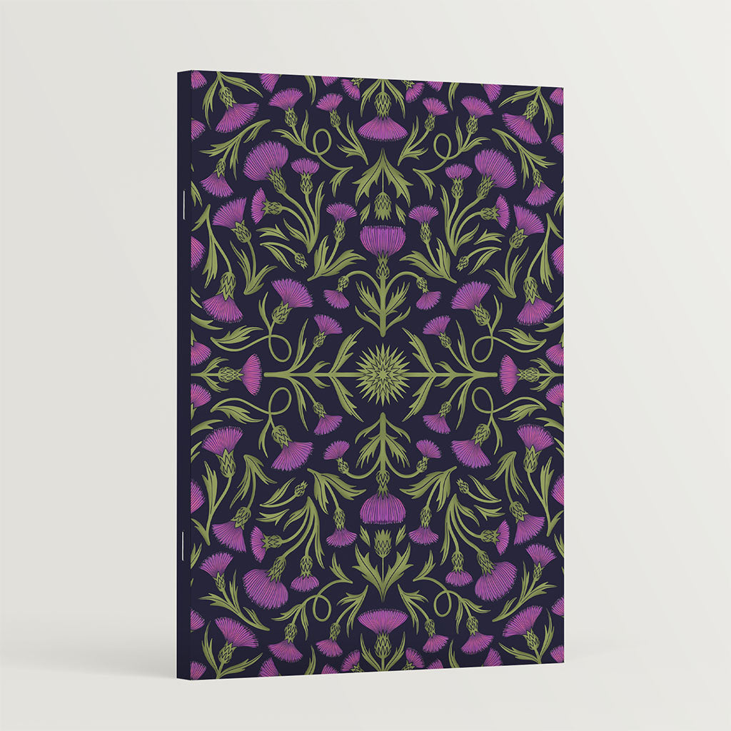 The Heritage Thistles Notebook features lush, symmetrical purple thistle flowers and green stems on a dark background, offering a vintage-inspired floral design ideal for journaling enthusiasts.