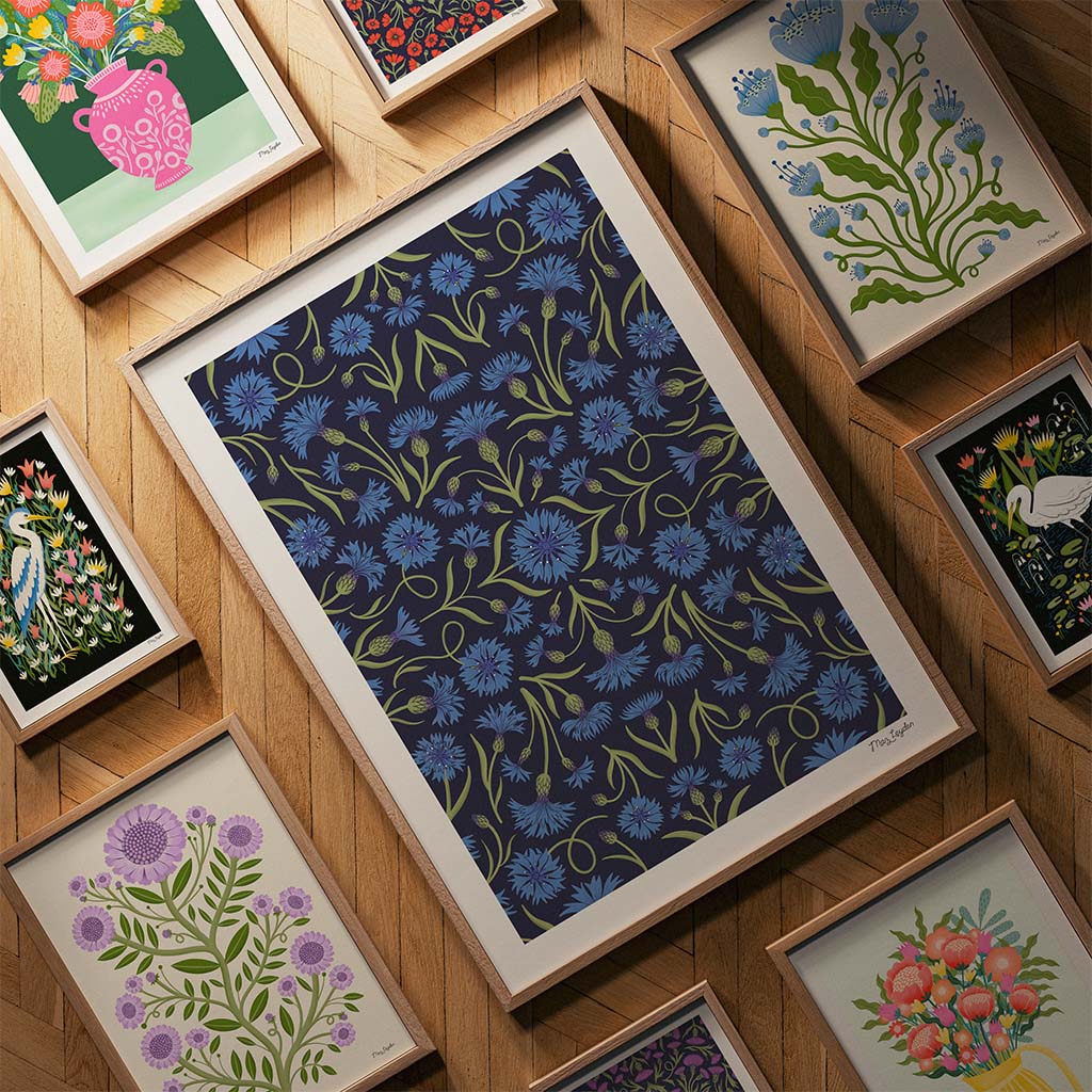 Framed floral illustrations arranged on a wooden herringbone floor, with a large dark blue print featuring blue flowers at the center.