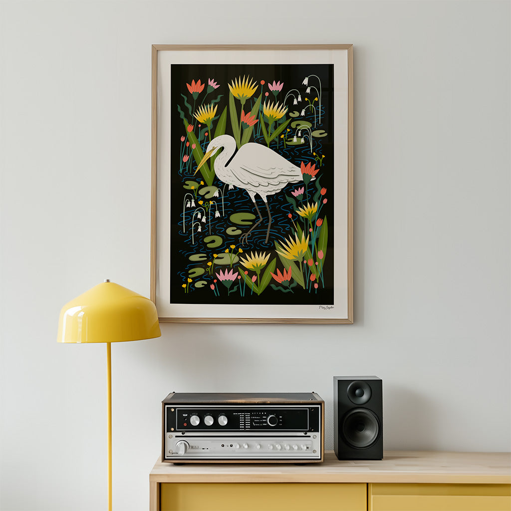 A Great Egret Art Print, featuring a white bird among lily pads and flowers, hangs above a yellow dresser with a speaker, stereo, and yellow lamp—ideal nature-themed decor for any space.