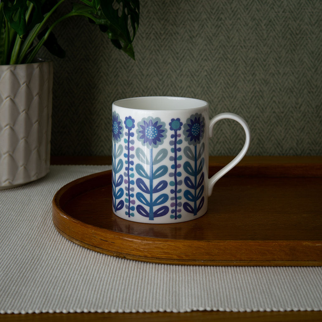 The Vintage Navy Blue Mug with a blue and purple floral pattern sits on a wooden tray beside a potted plant on a textured surface.