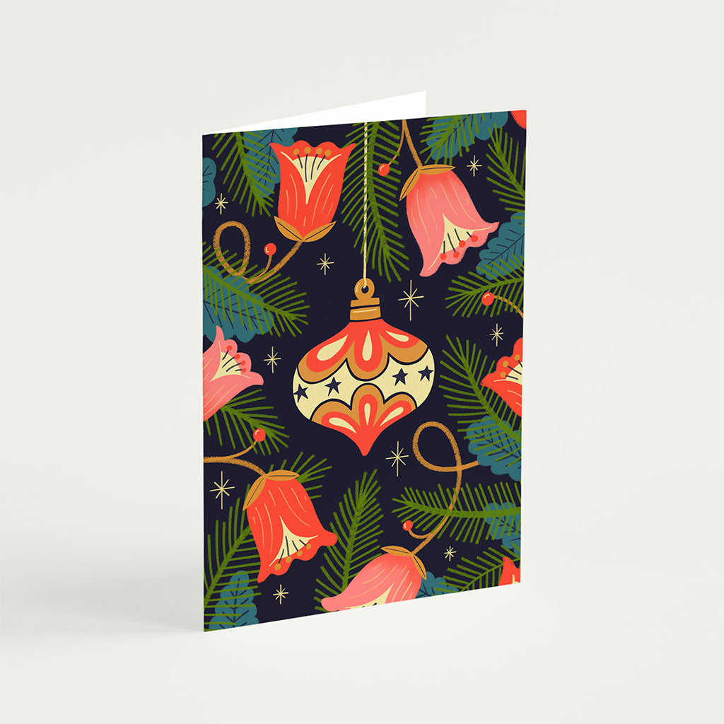 The Bauble Christmas Card features red flowers, green pine branches, gold stars, and a gold ornament on a dark background for festive holiday style.