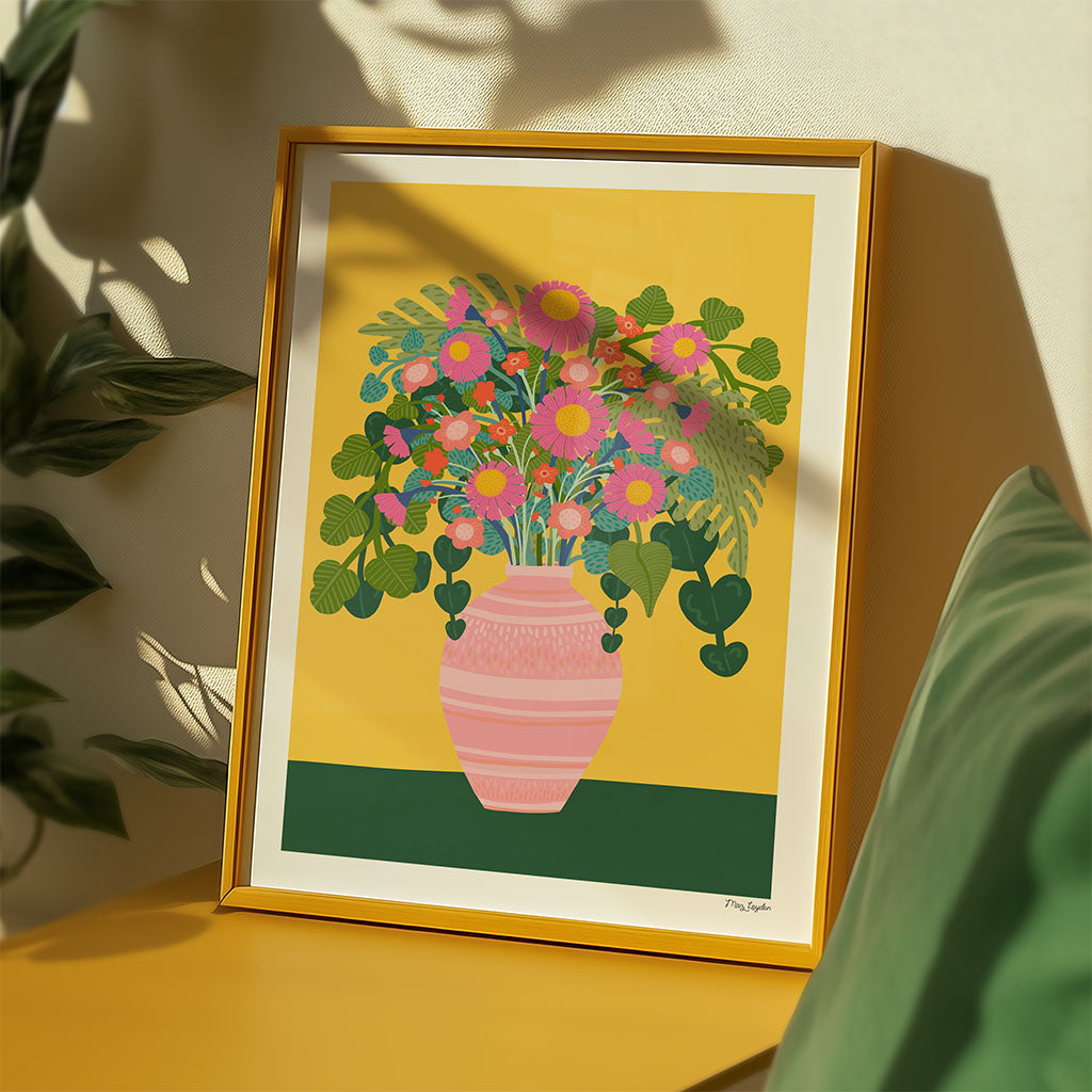 A Flower Vase Art Print features a luxury pink vase filled with pink blooms and green leaves, set on a green surface against a mustard yellow background.
