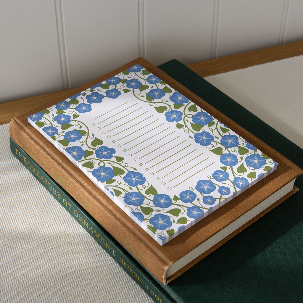 The Heavenly Blue Floral Notepad features a rectangular design with a blue and green floral border and lined centre, ideal for shopping lists or organising daily tasks, displayed on a plain white background.