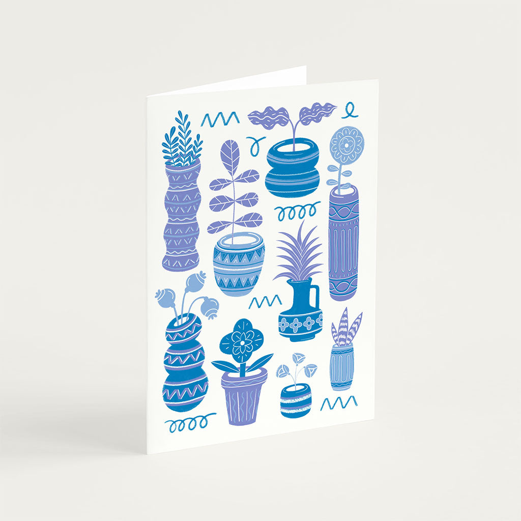The Blue Pots & Plants Greetings Card stands upright and features stylish blue and purple illustrations of potted cacti and succulents on a white background.