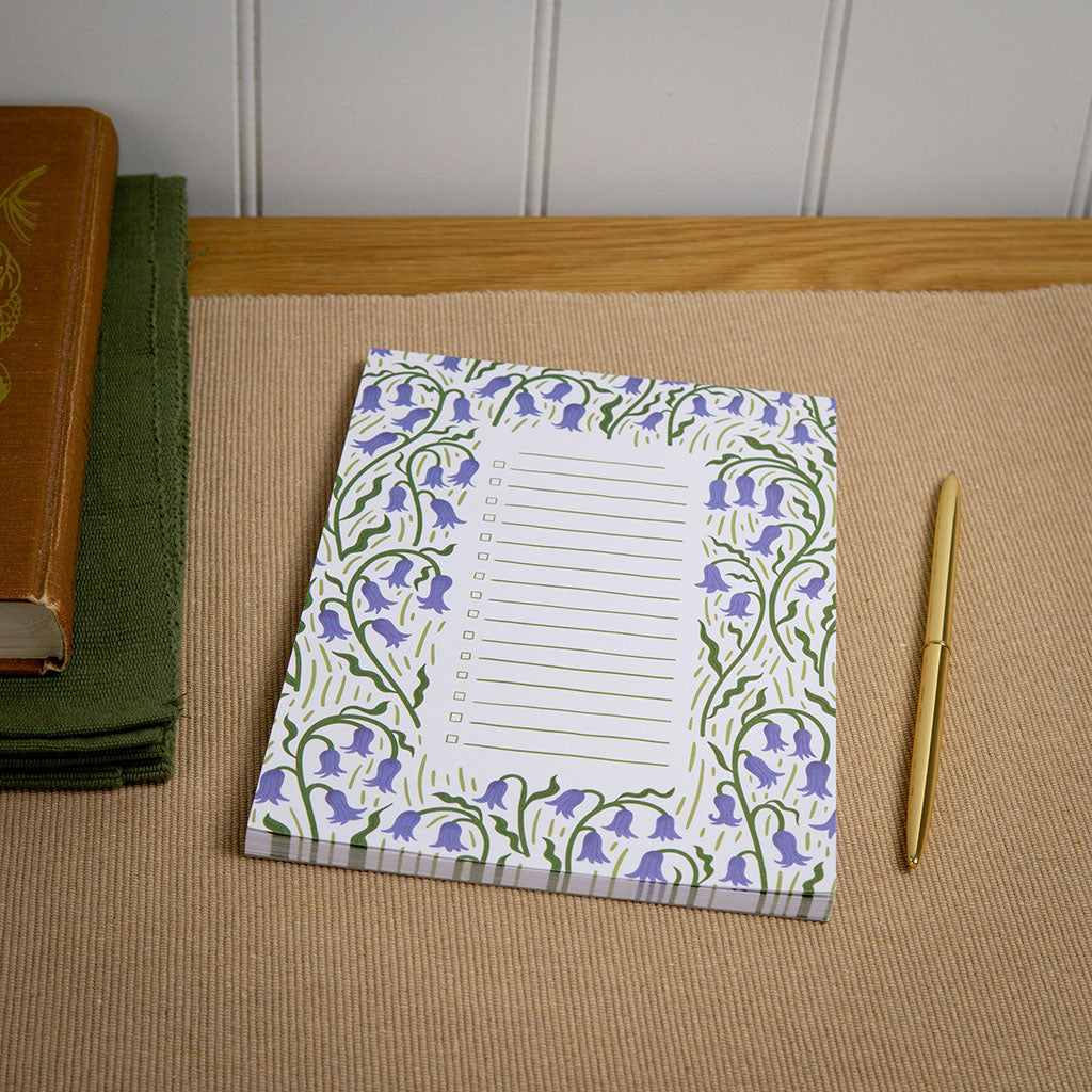 A checklist notepad with bluebell illustrations is on a desk with stationery.