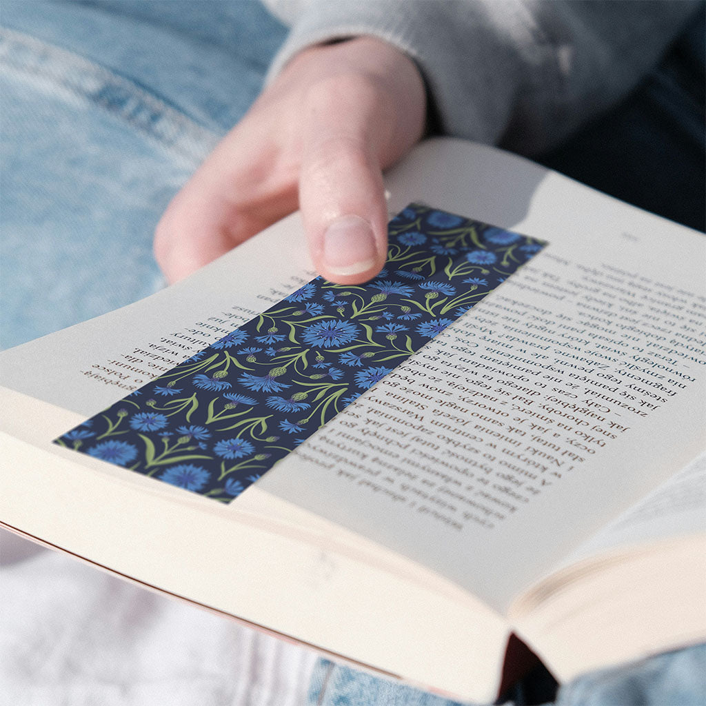 The Heritage Cornflower Bookmark features a symmetrical floral pattern with blue flowers and green leaves on a dark background, inspired by 19th-century pattern design.