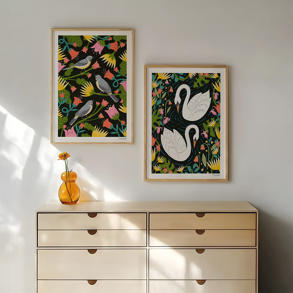 A wooden dresser with a single orange vase and flower stands against a wall, above which hangs a set of 2 British Bird art prints that show grey wagtails and white swans.