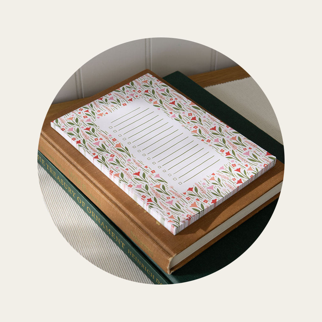 A checklist notepad with an illustrated floral motif sitting on top of two books on a tabletop.