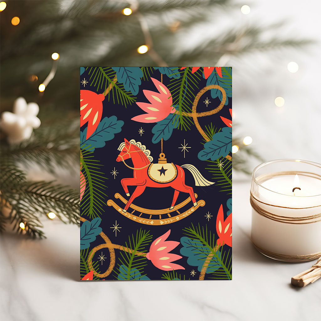 The Christmas Card Set features a red rocking horse amongst green leaves and pink flowers on a dark background, printed using vegetable-based inks on sustainably sourced card stock.