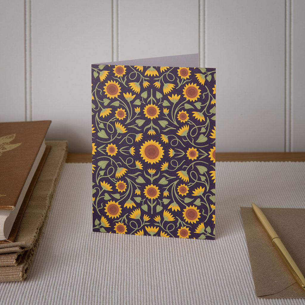 A sunflower greetings card with 19th century style pattern, displayed on a wooden table.