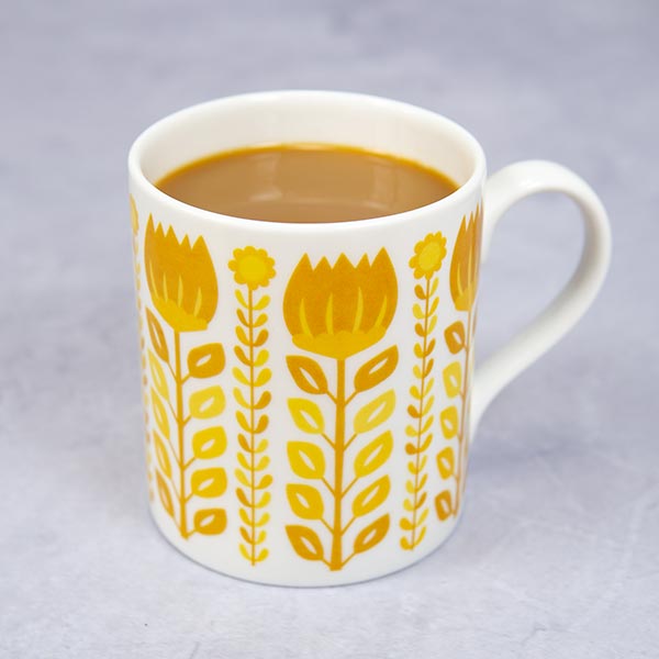 A mid-century style fine bone china mug with a yellow floral patterned design sits on a marble tabletop.