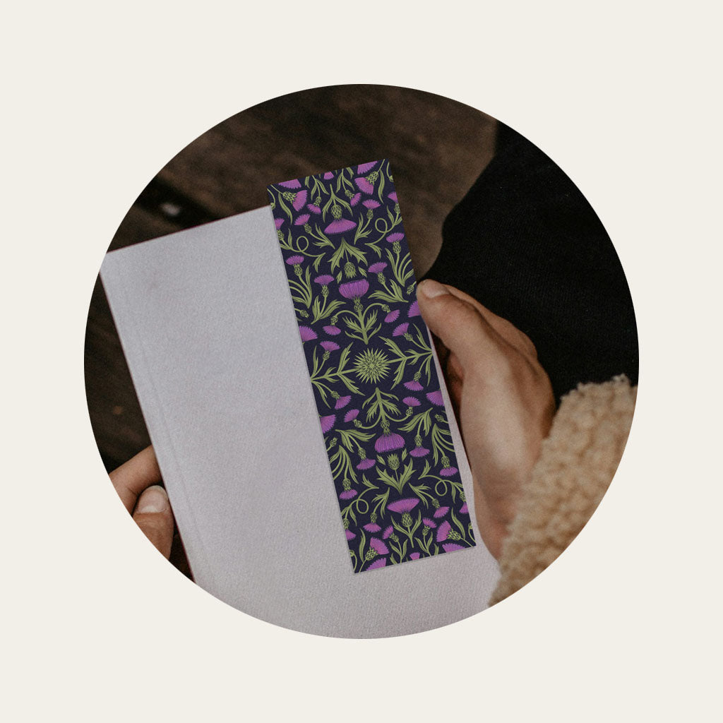 A woman's hands holding a book with a floral patterned bookmark on top of it.