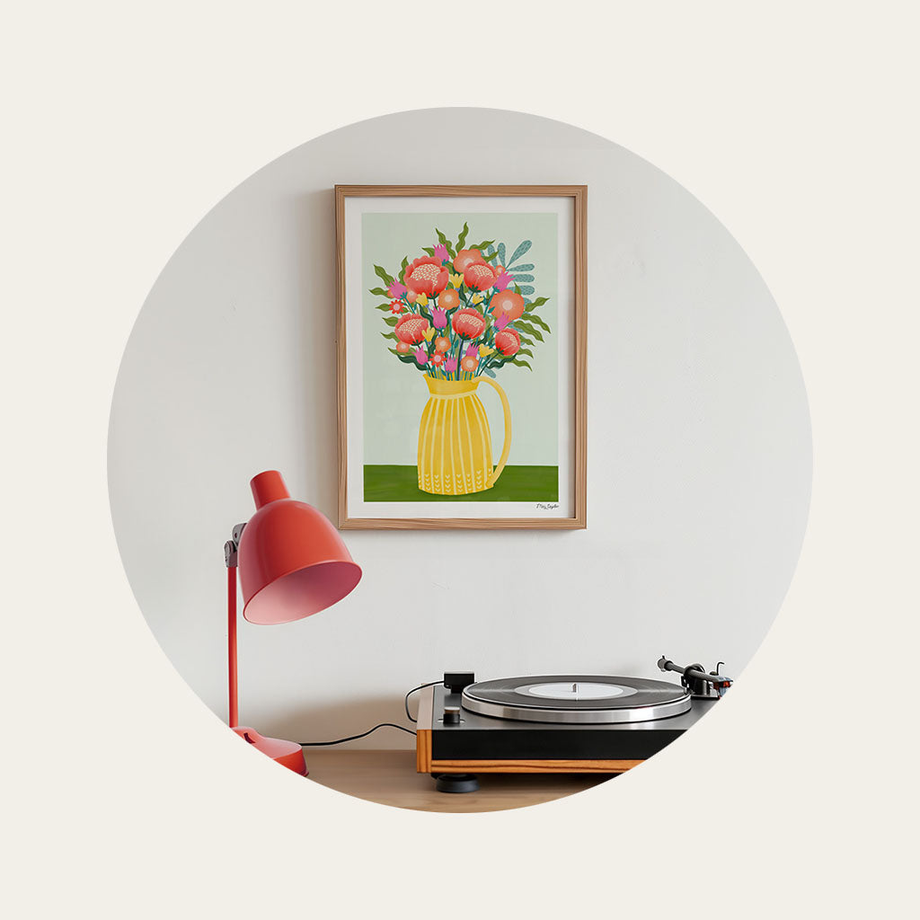 A framed art print of an illustrated vase of flowers displayed on a wall above a record player on a cabinet.