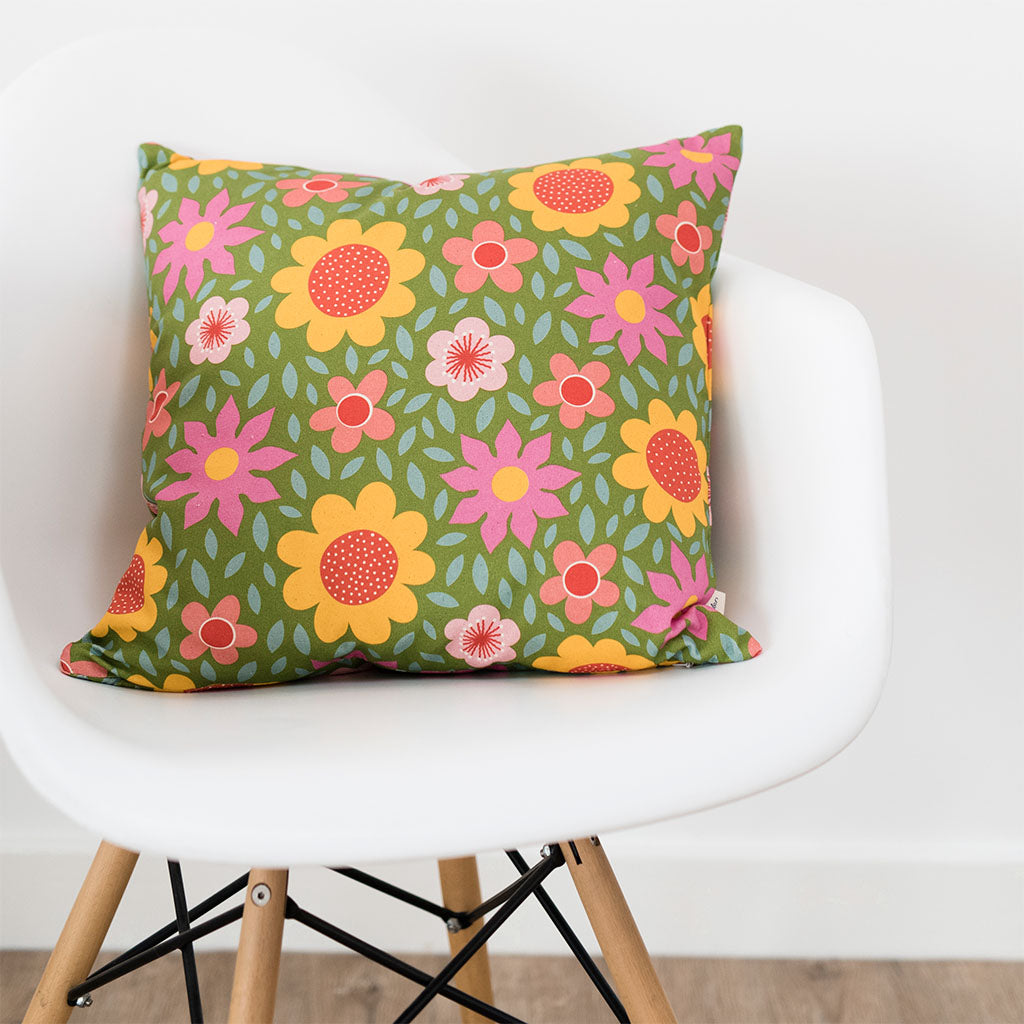 The Lawn Daisies Cushion Cover features a retro, colorful floral pattern on a green background. Made from organic cotton, this square cover adds charm and comfort to any space—perfect for floral cushion lovers.