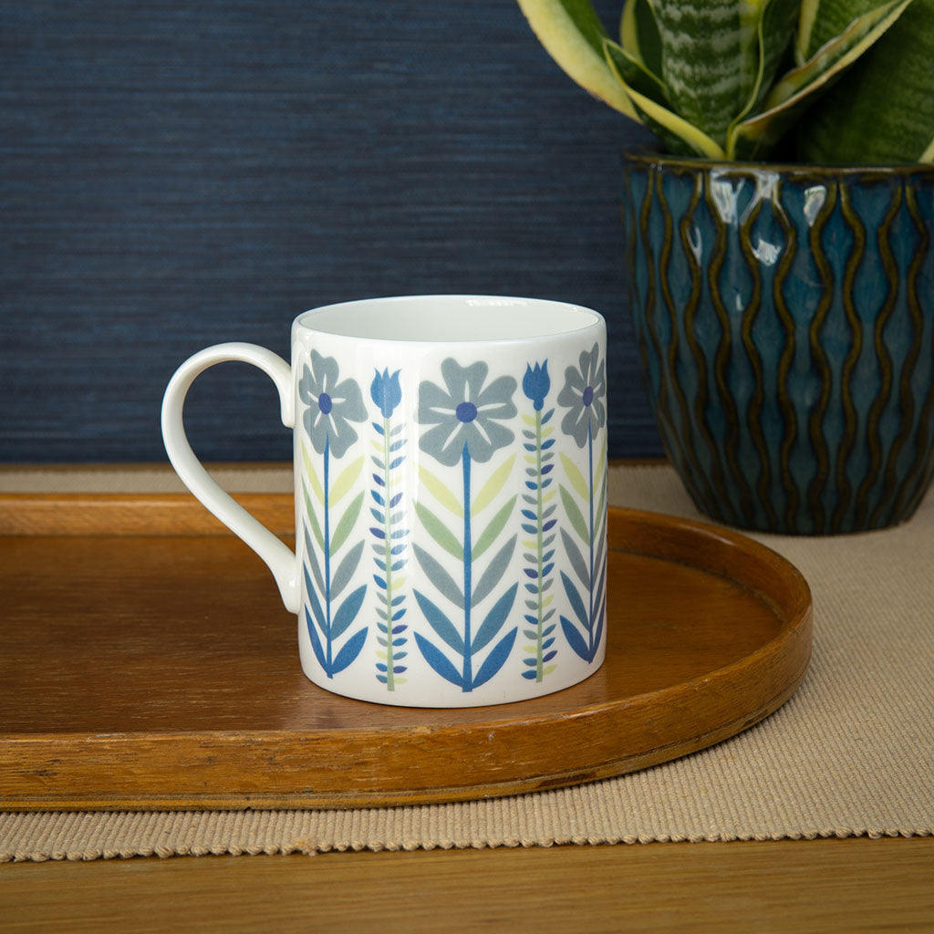 The Vintage Blue Mug is a fine bone china mug, decorated with a mid-century style pattern of illustrated blue and green flowers, stems, and leaves.