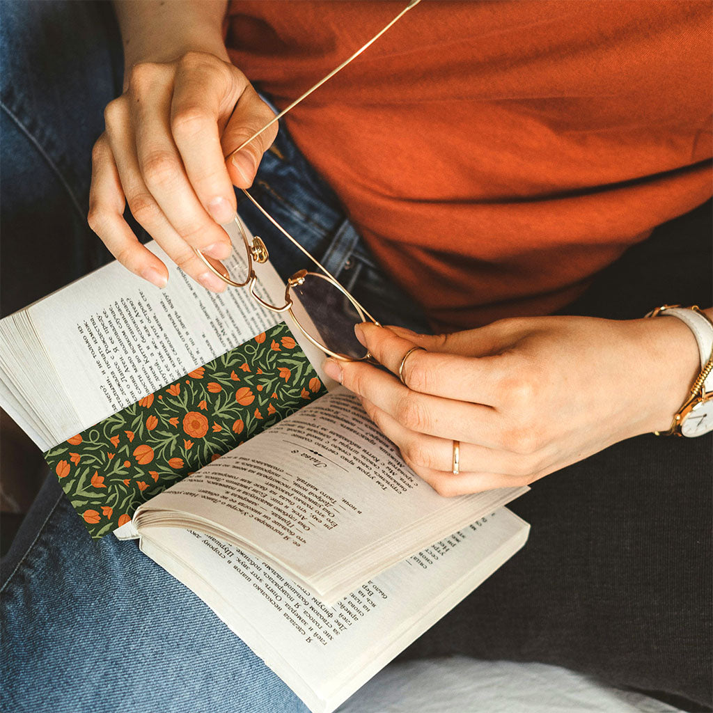 A woman holds glasses above an open book marked with the Heritage Tulip Bookmark.