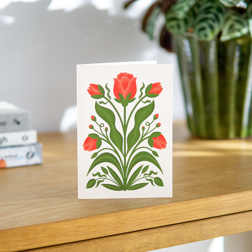 The Red Tulips Greetings Card features illustrated red tulips with green leaves on a natural cream background, making it an ideal choice for botanical enthusiasts.