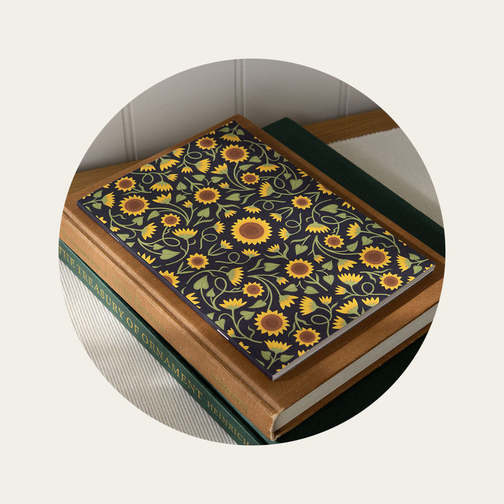 A notebook with a sunflower design on the cover sits on top of a stack of books on a table.