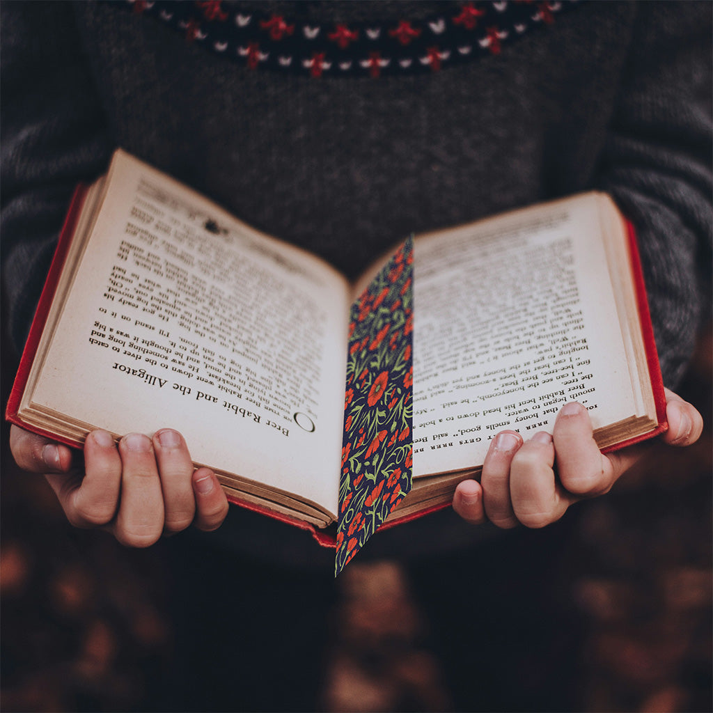 The Heritage Poppy Bookmarks feature a symmetrical floral design with red flowers and green leaves on a dark background, crafted from sustainable materials.