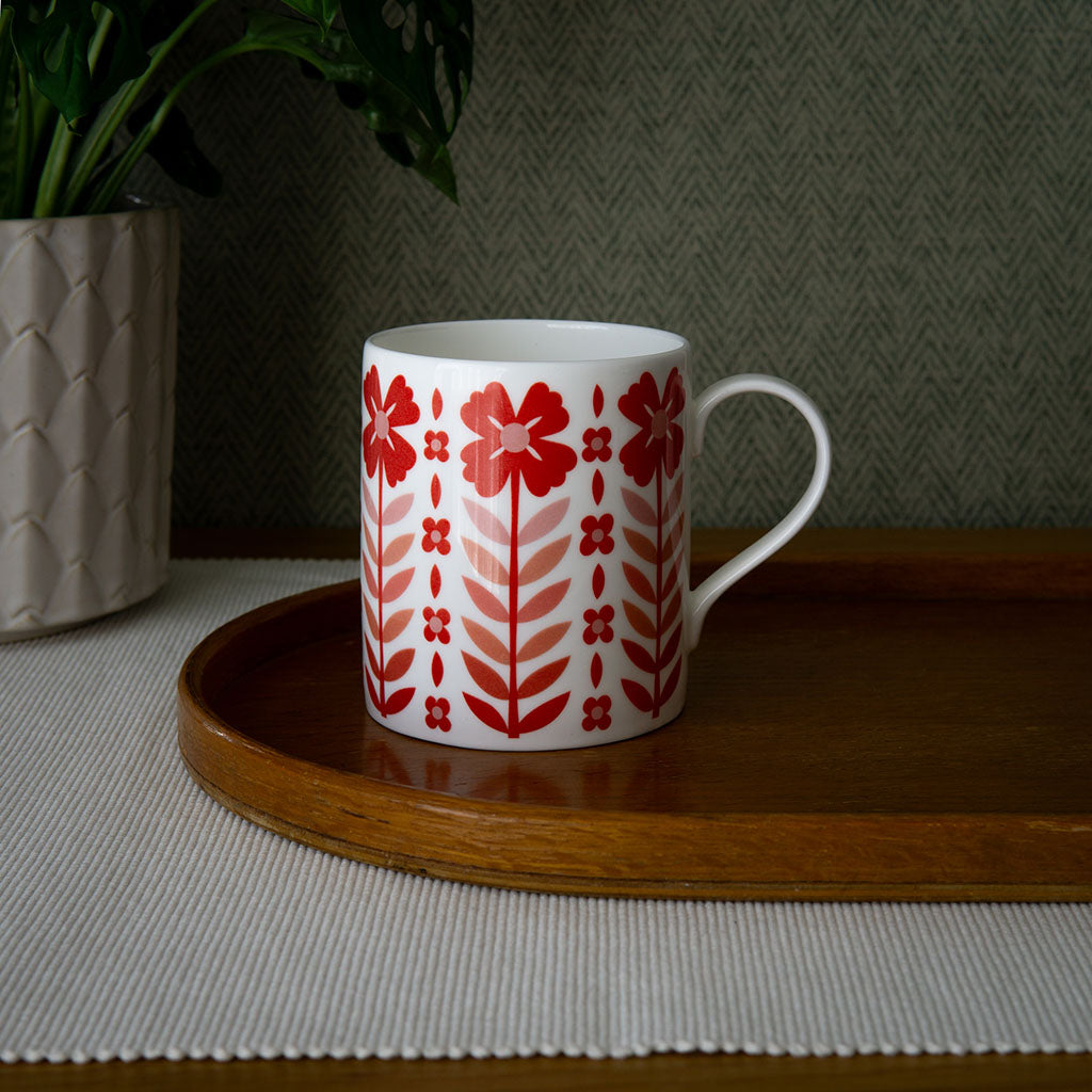 The Vintage Red Mug is a white fine bone china mug with a vintage style and a pattern of red flowers and leaves arranged in vertical rows.