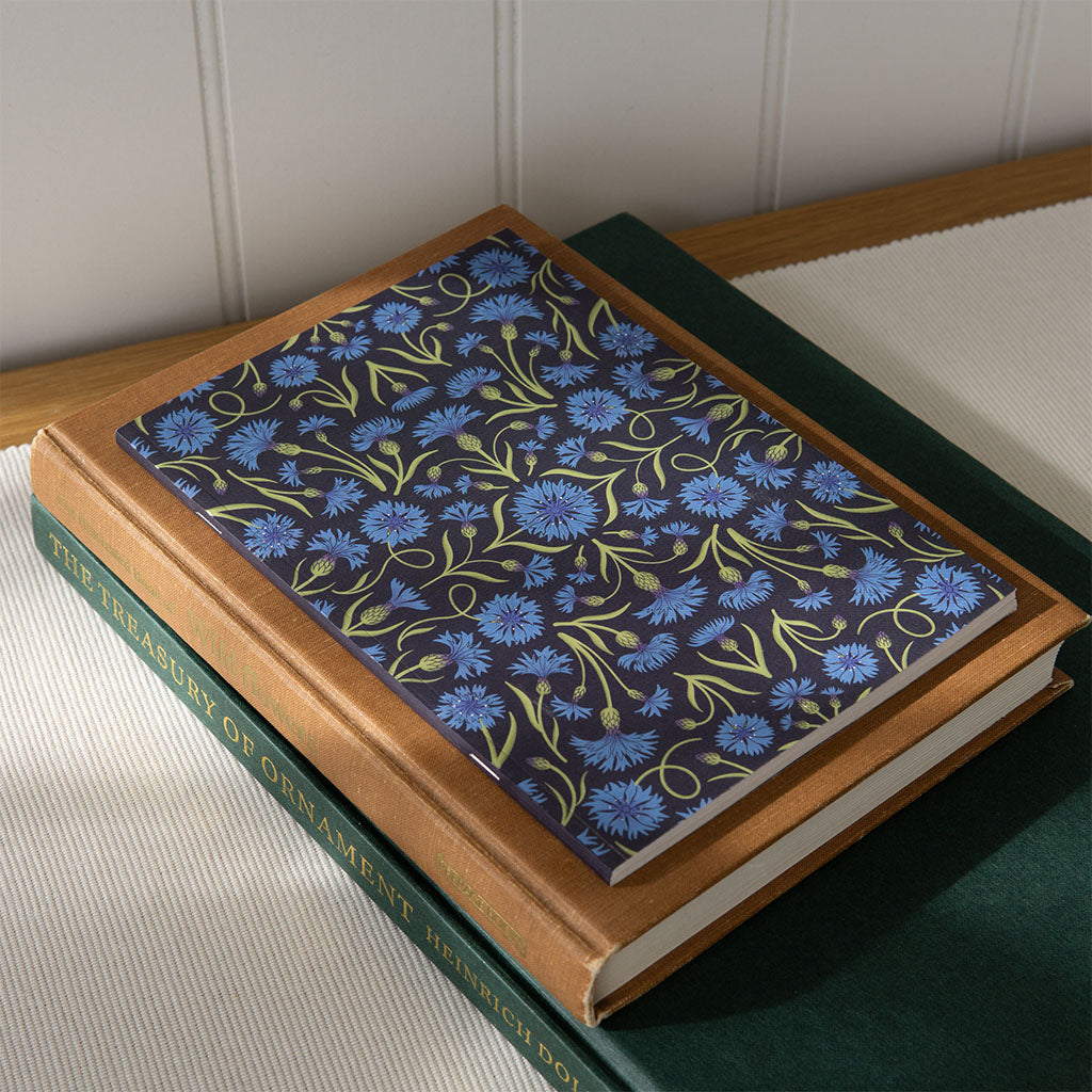 A cornflower pattern journal with a vintage style design with a stack of art books on a desk.