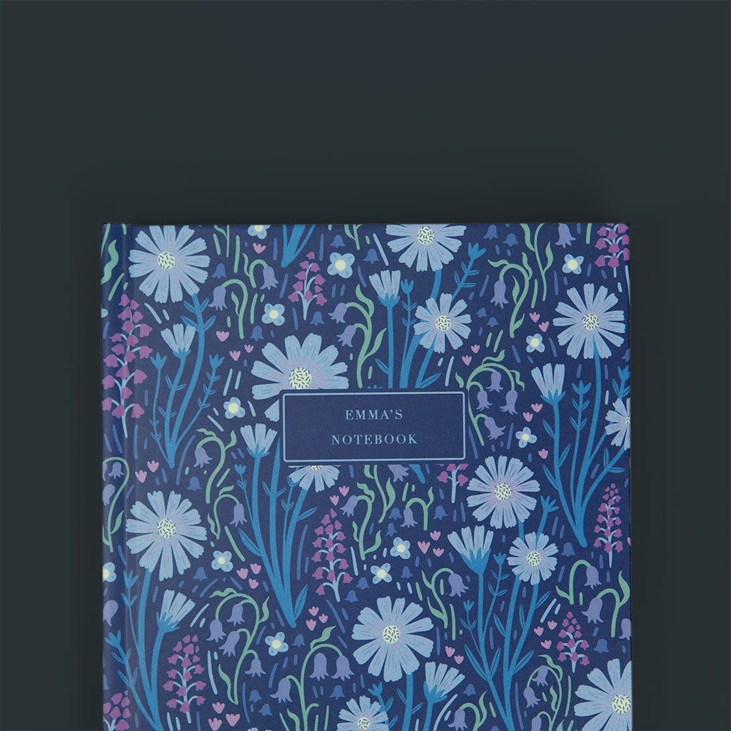 Close up of the navy blue floral patternned cover of a personalised notebook, with customised notebook text. It sits on a dark blue background.