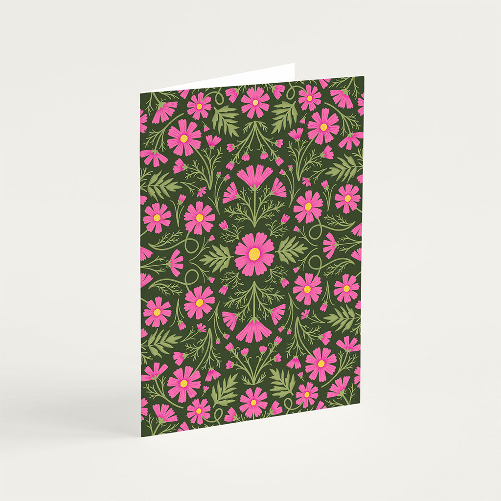 The Heritage Cosmos Greetings Card stands upright, showcasing pink flowers and green leaves on a dark background, printed with vegetable-based inks.