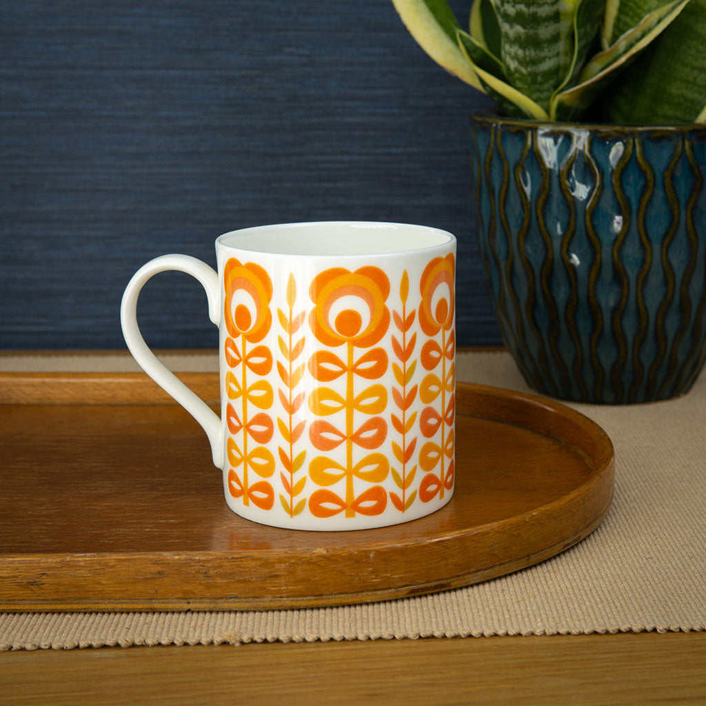 The Vintage Orange Mug is a retro-style white ceramic mug made in the UK, featuring an orange and yellow floral pattern on a plain white background.