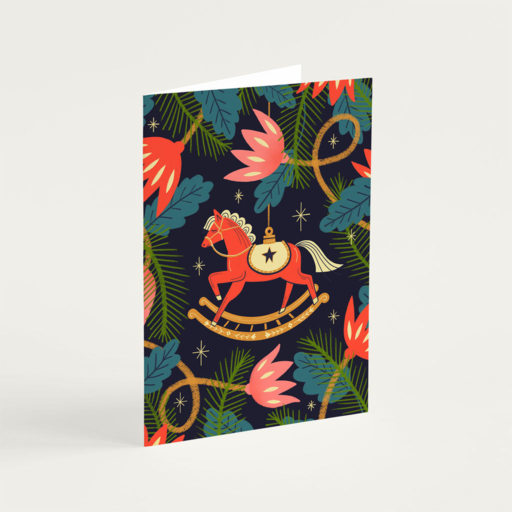 The Christmas Card Set features a red rocking horse amongst green leaves and pink flowers on a dark background, printed using vegetable-based inks on sustainably sourced card stock.