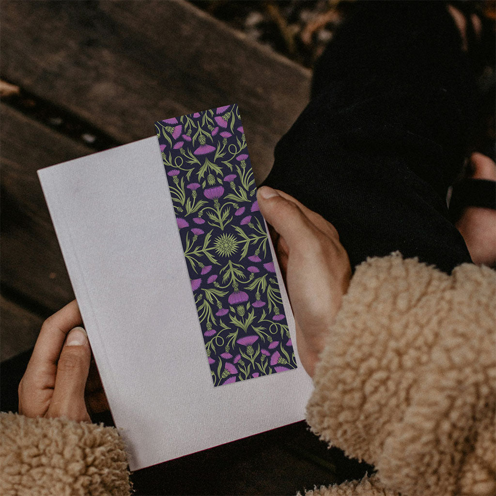The Heritage Thistle Bookmark features a symmetrical pattern of green stems and purple thistle flowers—a thoughtful, inspired gift for book lovers who appreciate both literary charm and botanical beauty.