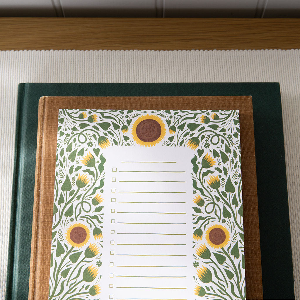 The Sunflowers Floral Notepad is a rectangular checklist pad with a sunflower and green leaf border, blank lines, and checkboxes, ideal for organising your daily tasks in style.
