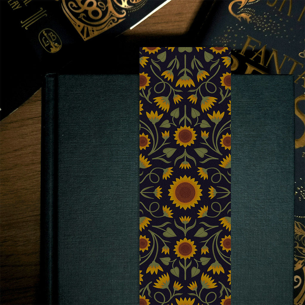 A perfect gift for book lovers, the Heritage Sunflower Bookmark features a symmetrical sunflower and foliage pattern in yellow, orange, and green on a dark background- radiating sunflower charm.