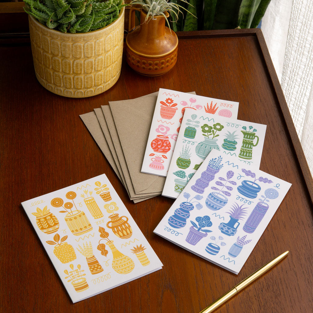 The Pots & Plants Greetings Card Set includes four retro cards featuring stylised vases and house plants in red, blue, yellow, and green colour schemes on a neutral background.
