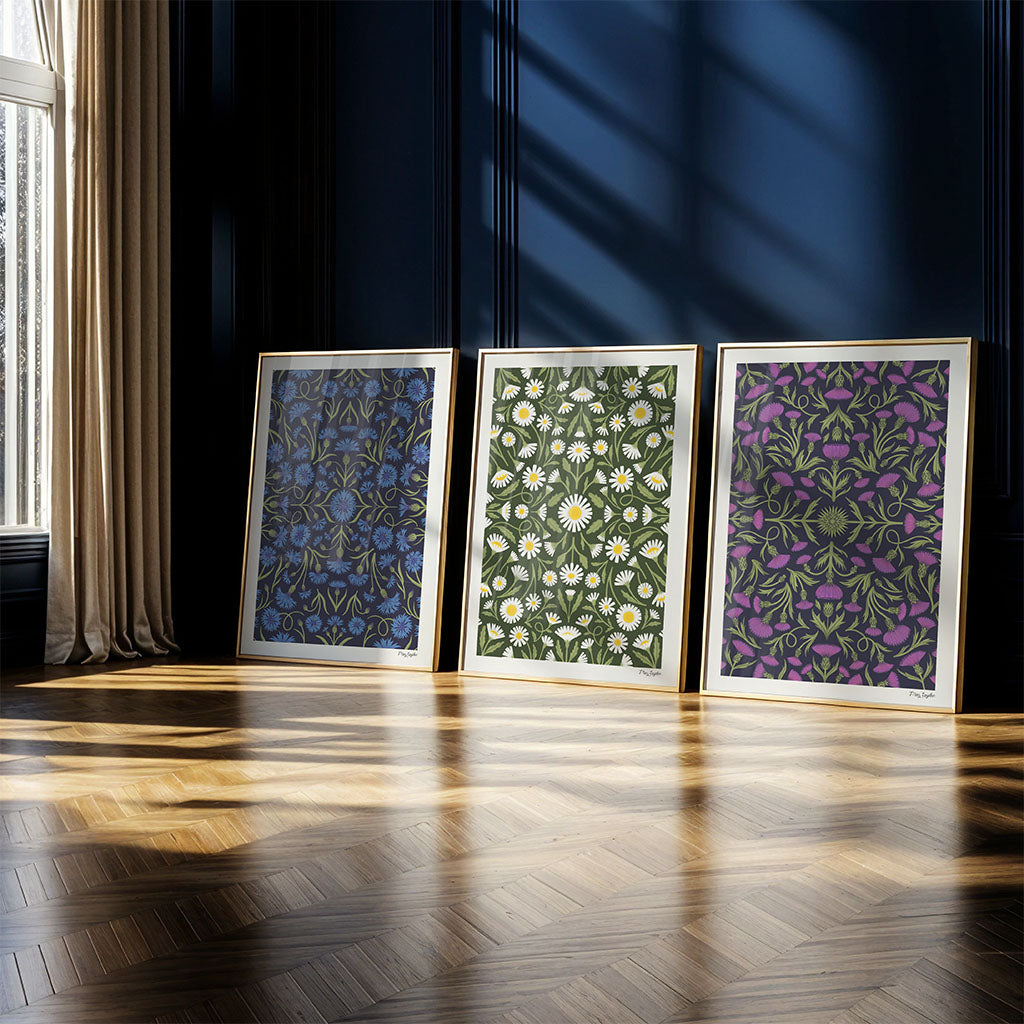 The Heritage set of 3 art prints, featuring timeless botanical designs, is displayed propped against a dark blue wall in a sunlit room with wooden herringbone floor.