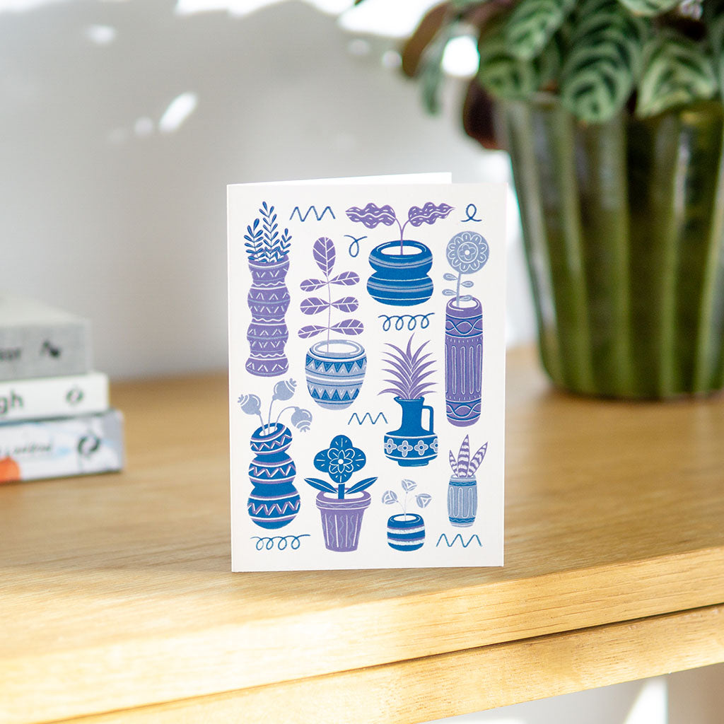 The Blue Pots & Plants Greetings Card stands upright and features stylish blue and purple illustrations of potted cacti and succulents on a white background.