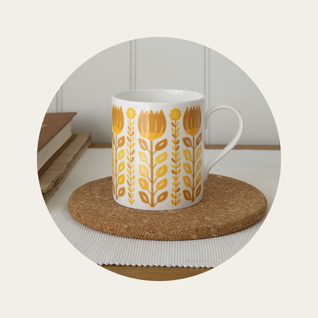 A fine bone china mug with a mid-century floral pattern sitting on a cork coaster on a wooden table.