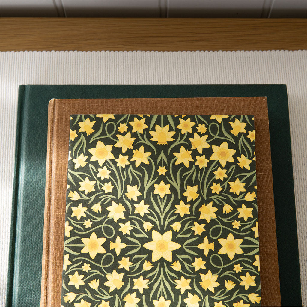 The Heritage Daffodils Notebook features a vintage-inspired cover with yellow daffodil flowers and green leaves on a dark background, perfect for journaling.