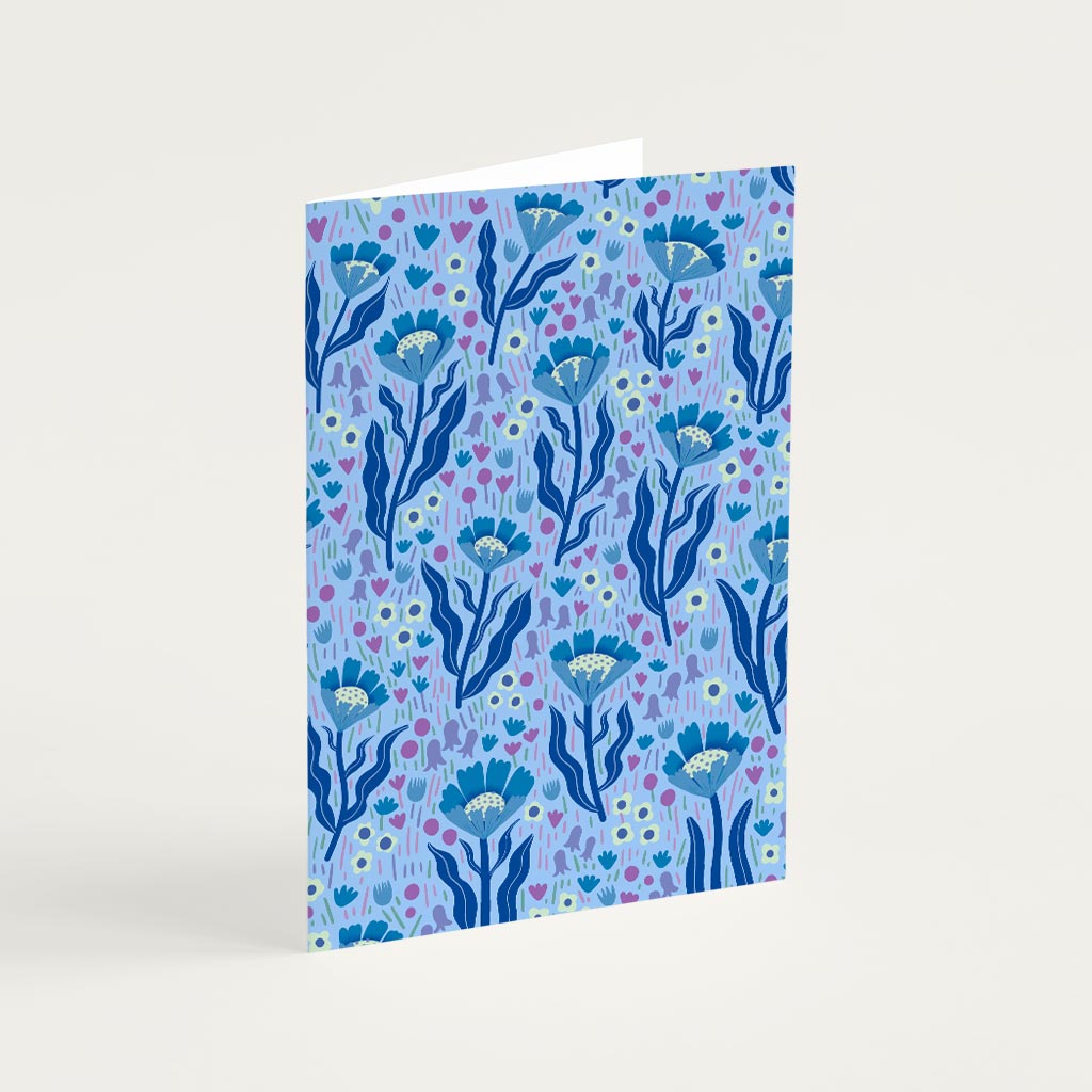 The Blue Wildflowers Greetings Card features a blue botanical pattern inspired by British wildflowers on a light purple background, with illustrated flowers and leaves.