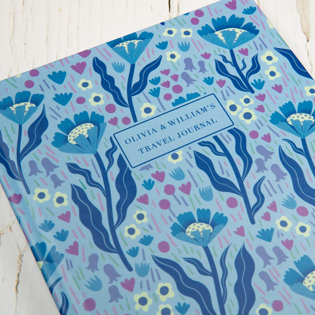 The Blue Wildflowers Personalised Notebook is a luxurious hardcover travel journal with a blue floral pattern inspired by British wildflowers and a custom text label section on the front cover.