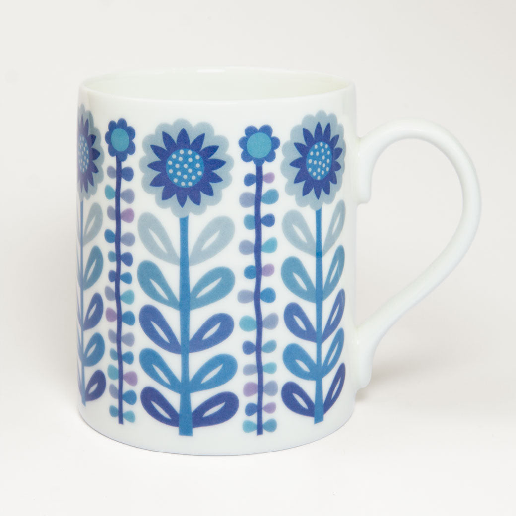 The Vintage Navy Blue Mug features a white ceramic body with blue and purple illustrated flowers and leaves in a retro design, adding mid-century charm to any kitchen. Displayed against a plain white background.