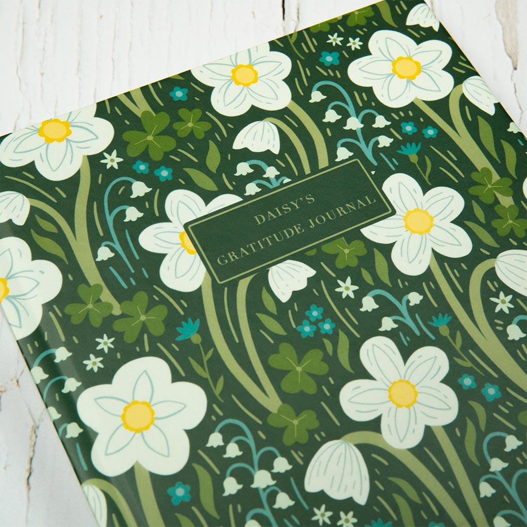 The Dark Green Wildflowers Personalised Notebook is a hardcover journal with a green floral cover featuring British wildflowers such as white daisies and wood anemones, perfect for daily reflections.