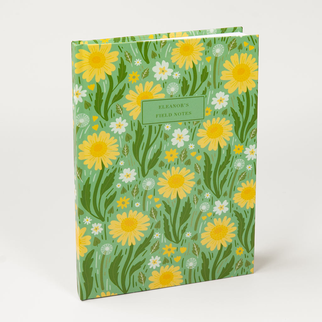 The Green Wildflowers Personalised Notebook features charming British wildflower illustrations, a yellow and white daisy pattern, and a customisable text label on the cover.