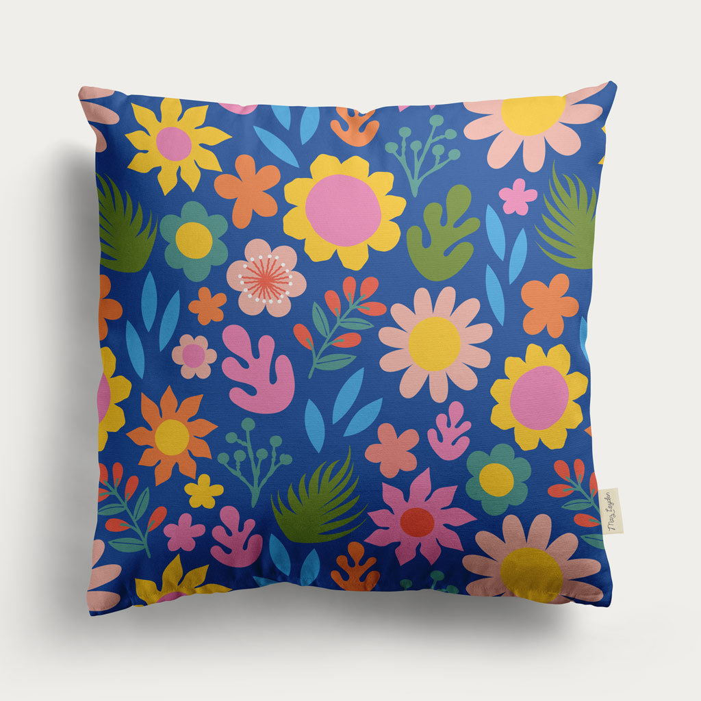 The Flower Patch Cushion Cover features a vibrant floral pattern with pink, yellow, orange, and green flowers on a dark blue background—perfect for bringing vintage charm to your space.