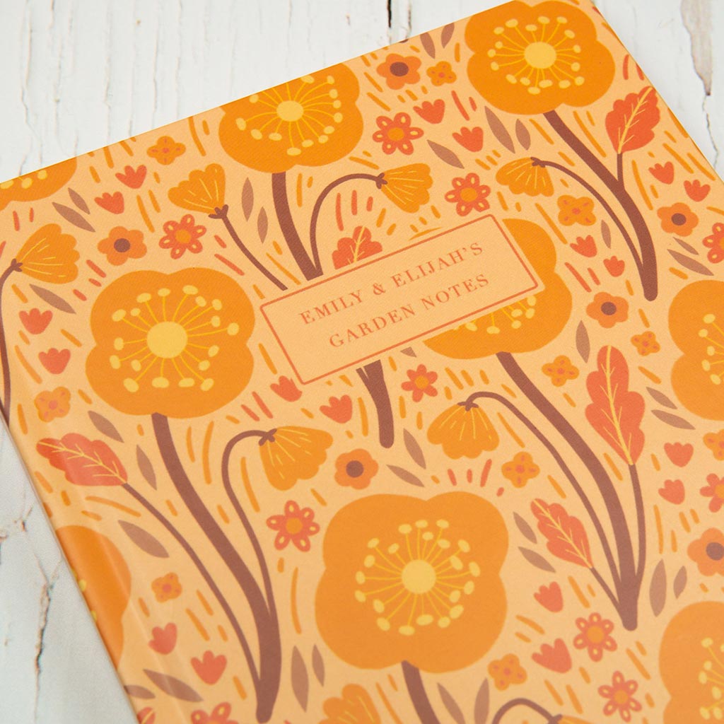 The Orange Wildflowers Personalised Notebook features charming British wildflower illustrations, an orange and yellow floral pattern, and a customisable cover label.