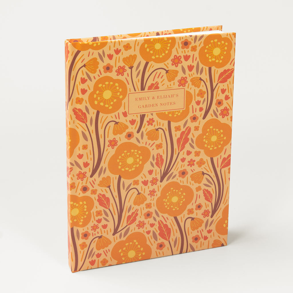 The Orange Wildflowers Personalised Notebook features charming British wildflower illustrations, an orange and yellow floral pattern, and a customisable cover label.
