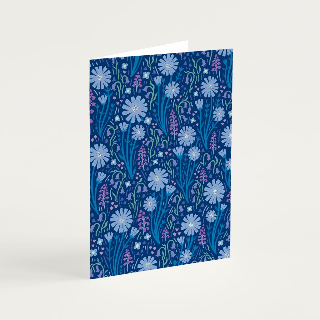 The Navy Blue Wildflowers Greetings Card stands upright with a navy blue background, decorated with white daisies and small purple wildflowers for an elegant floral touch.