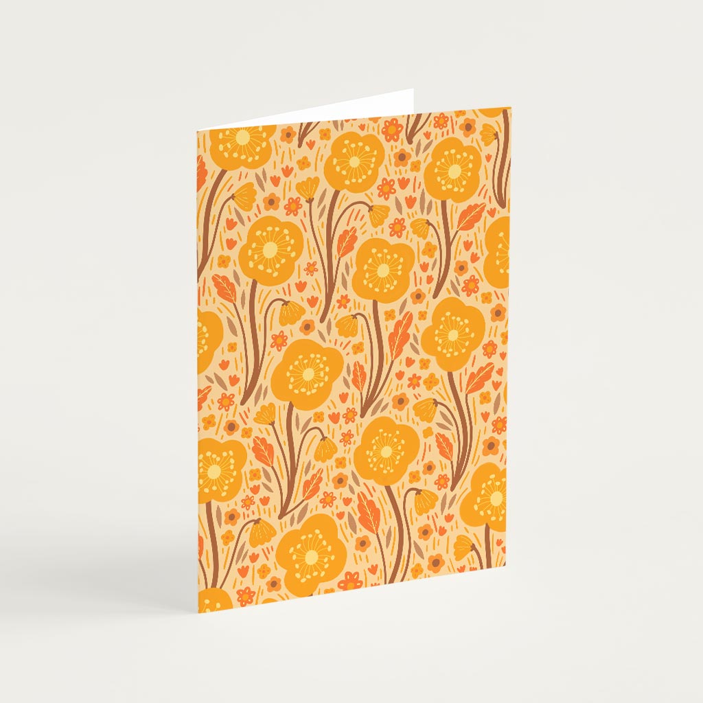 The Orange Wildflowers Greetings Card stands upright, showcasing a yellow and orange floral design with illustrated botanical British wildflowers and leaves on a beige background.