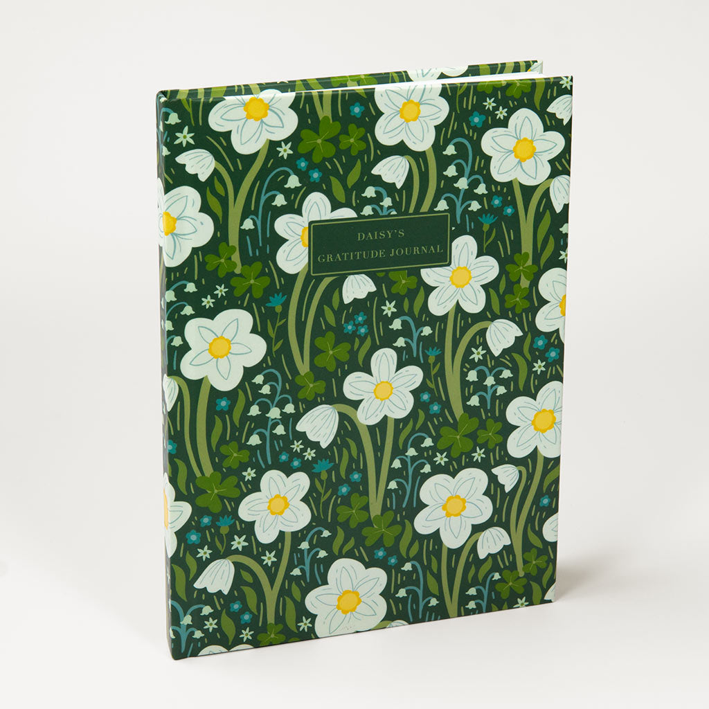 The Dark Green Wildflowers Personalised Notebook is a hardcover journal with a green floral cover featuring British wildflowers such as white daisies and wood anemones, perfect for daily reflections.